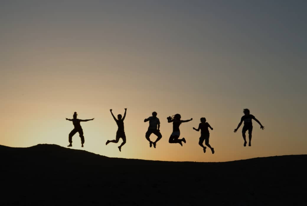 丘の上で沈む太陽を背にしてジャンプする六人